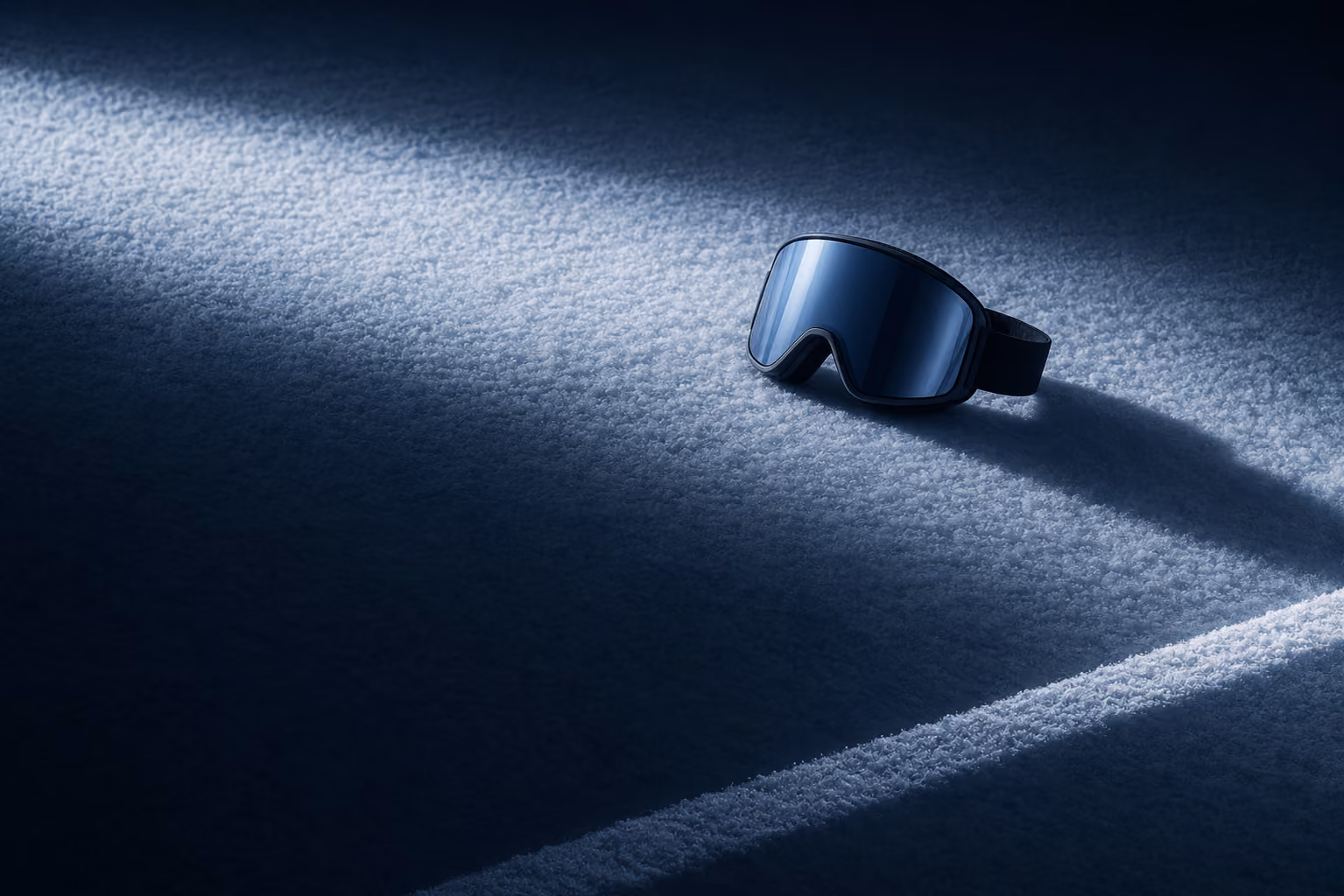 Schwarze Skibrille liegt im Licht auf verschneitem Boden mit Schatten.