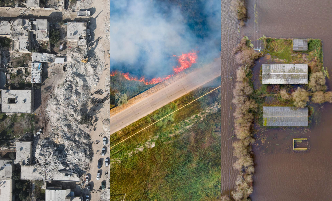 Aerial view of a wildfire burning near a road, showing flames and smoke within a wooded area adjacent to a paved street.