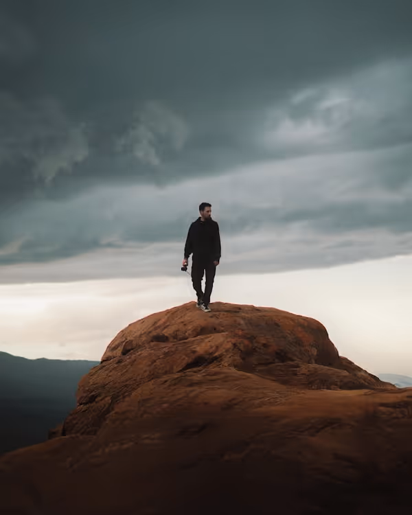 Man stands atop a rock, under a stormy sky.