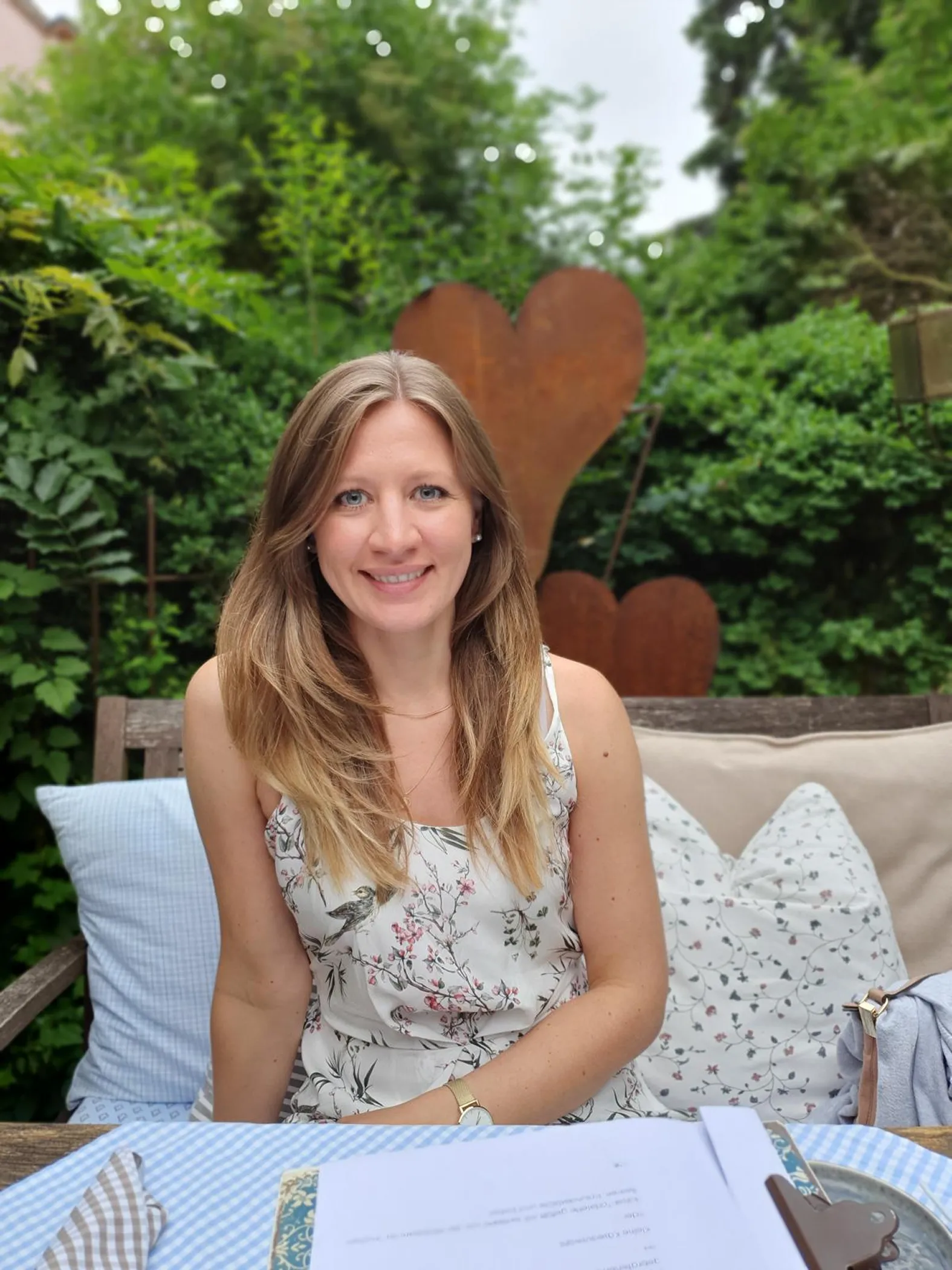Anne Hagelstein sitzt im Garten mit grünen Pflanzen im Hintergrund.