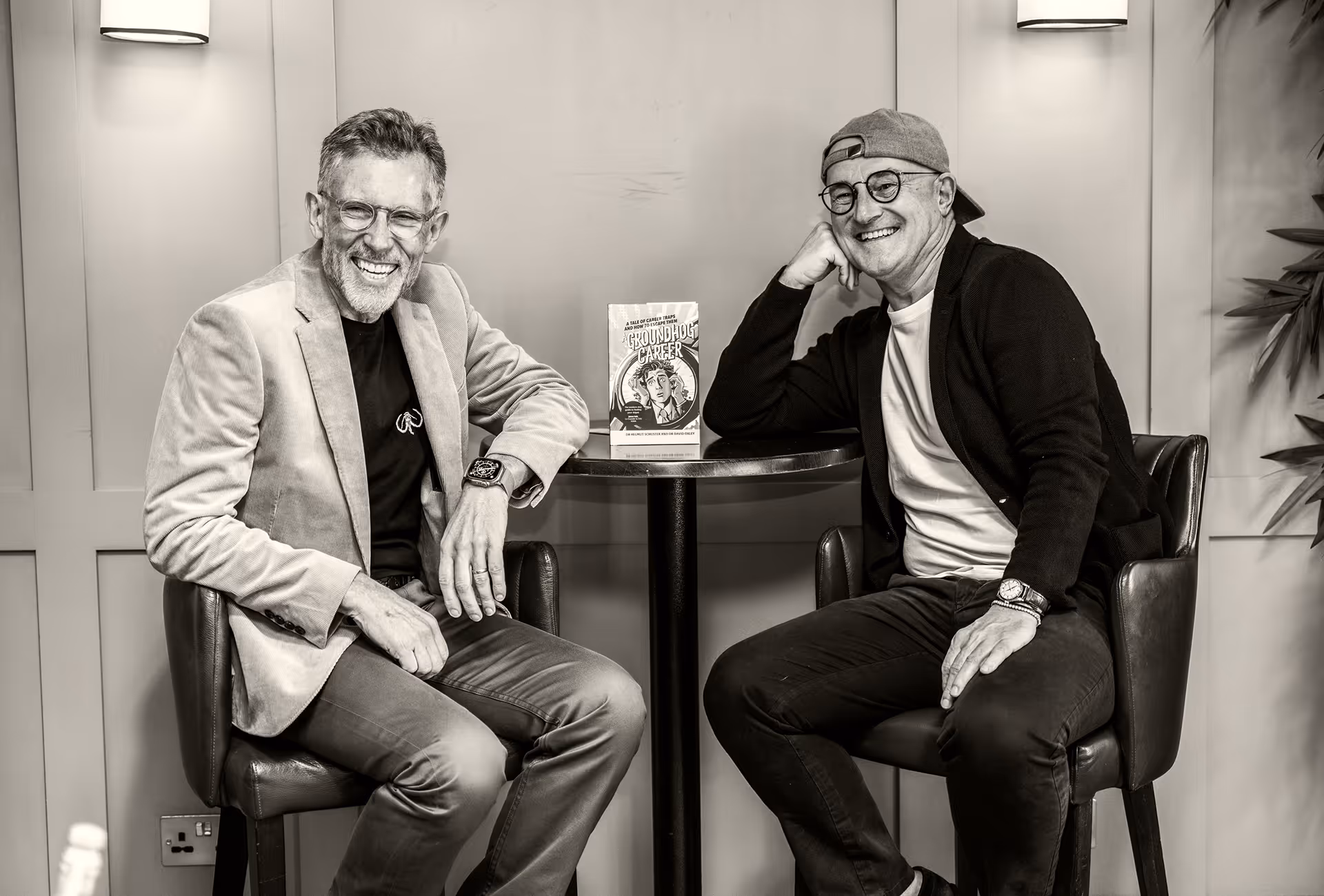 Dr Schuster and Dr Oxley sitting at a coffee table with their book "A groundhog career"