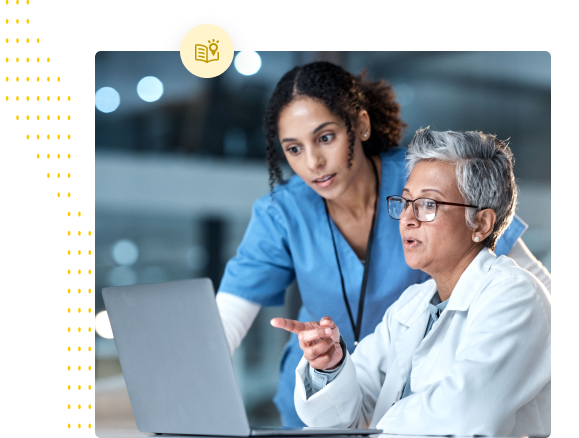Two female medical professionals, one older with glasses and one younger, looking at a laptop screen and discussing something.