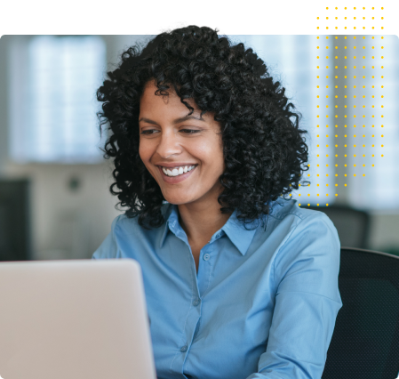 Smiling woman with curly hair wearing a blue shirt working on a laptop in an office.