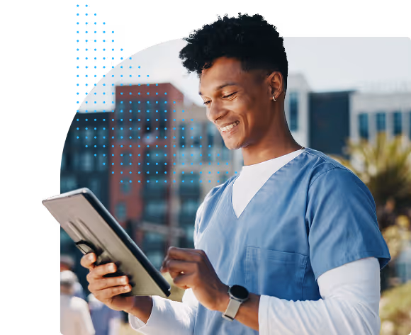 Smiling young male healthcare worker wearing blue scrubs and a smartwatch, holding and using a tablet outdoors.