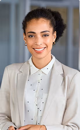 Smiling professional woman with curly hair in a beige blazer and white polka-dot blouse standing indoors.