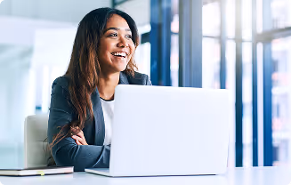 Smiling woman sitting at a desk with a laptop in a bright office.