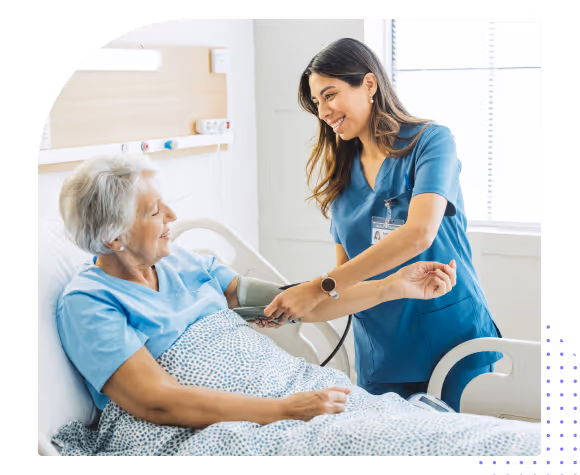 Nurse smiling and taking blood pressure of elderly female patient lying in hospital bed.