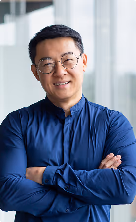 Smiling man with glasses and dark blue shirt standing with arms crossed in an office.
