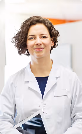 Female healthcare professional with curly hair wearing a white coat and holding a tablet.