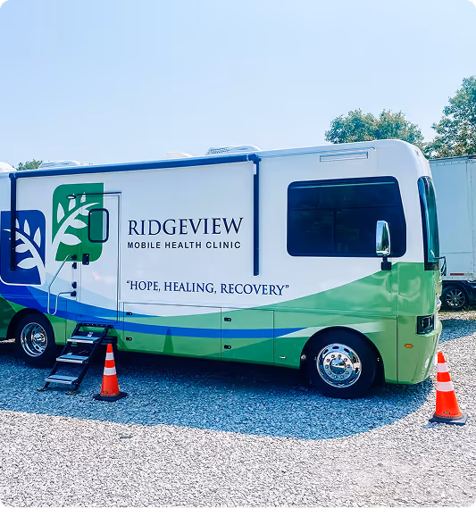 Ridgeview Mobile Health Clinic vehicle with green and blue design parked on gravel with two orange traffic cones.