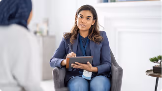 Woman in blazer holding tablet and pen, listening attentively to another person in a counseling session.