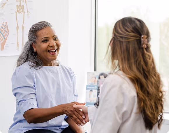 Smiling older woman patient shaking hands with female doctor in a medical office.