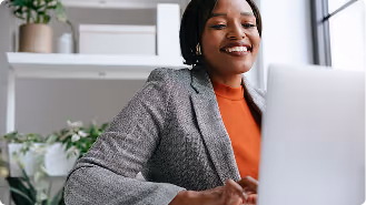 Smiling woman working on a laptop in a bright, modern office with plants in the background.