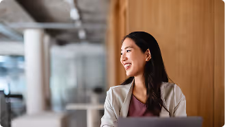 Smiling woman with long dark hair sitting in a modern office near wooden wall.