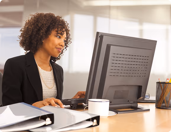 Businesswoman with curly hair working on a desktop computer at her office desk.