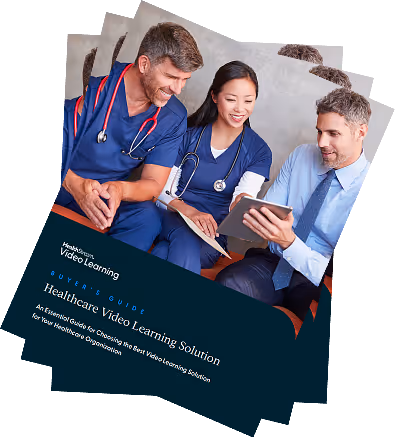 Three healthcare professionals, two in scrubs, viewing a tablet together and smiling.