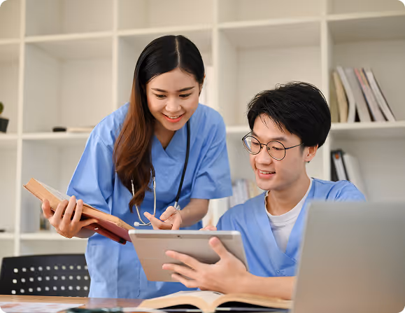 Two medical professionals in blue scrubs reviewing information on a tablet together.