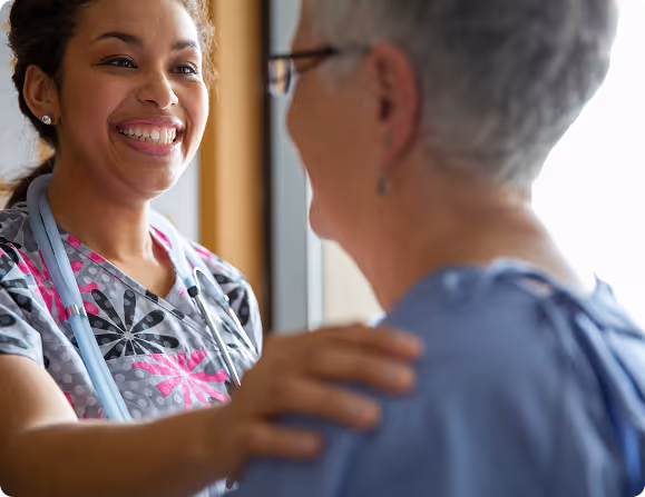 Nurse smiling and comforting an elderly patient by gently holding her shoulder.