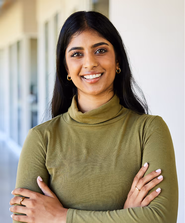 Confident woman in an olive green turtleneck smiling with arms crossed in a bright office corridor.