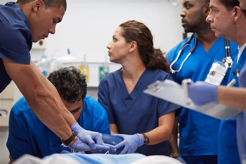 Medical team in blue scrubs working together on a patient in an emergency room setting.