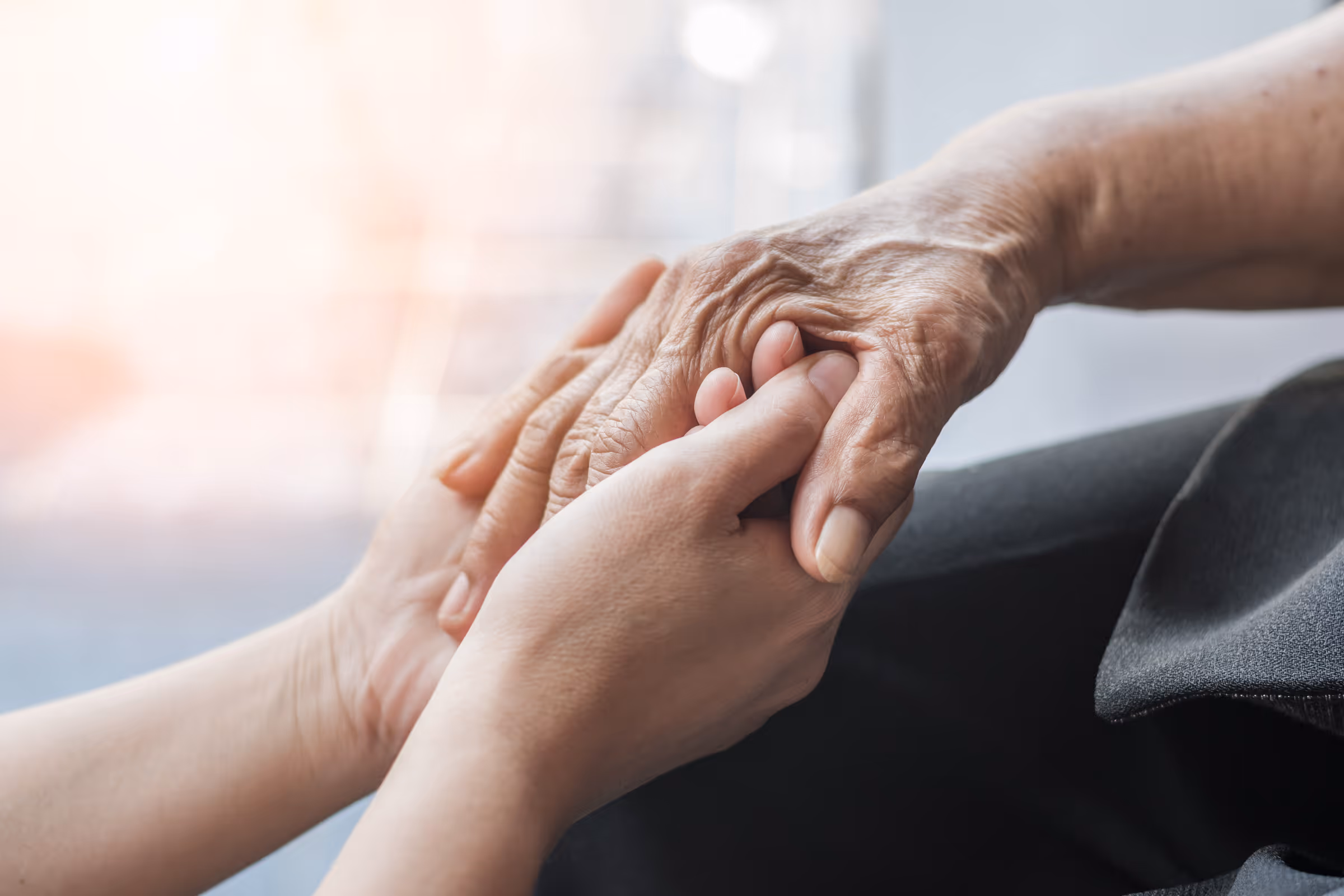 Younger hands gently holding an older person's wrinkled hands in a comforting gesture.