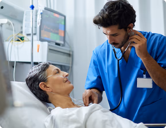 Doctor using stethoscope to listen to the chest of a patient lying in a hospital bed.
