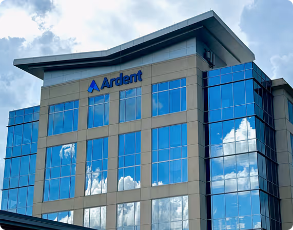 Modern office building with blue reflective windows showing clouds and sky, labeled Ardent.