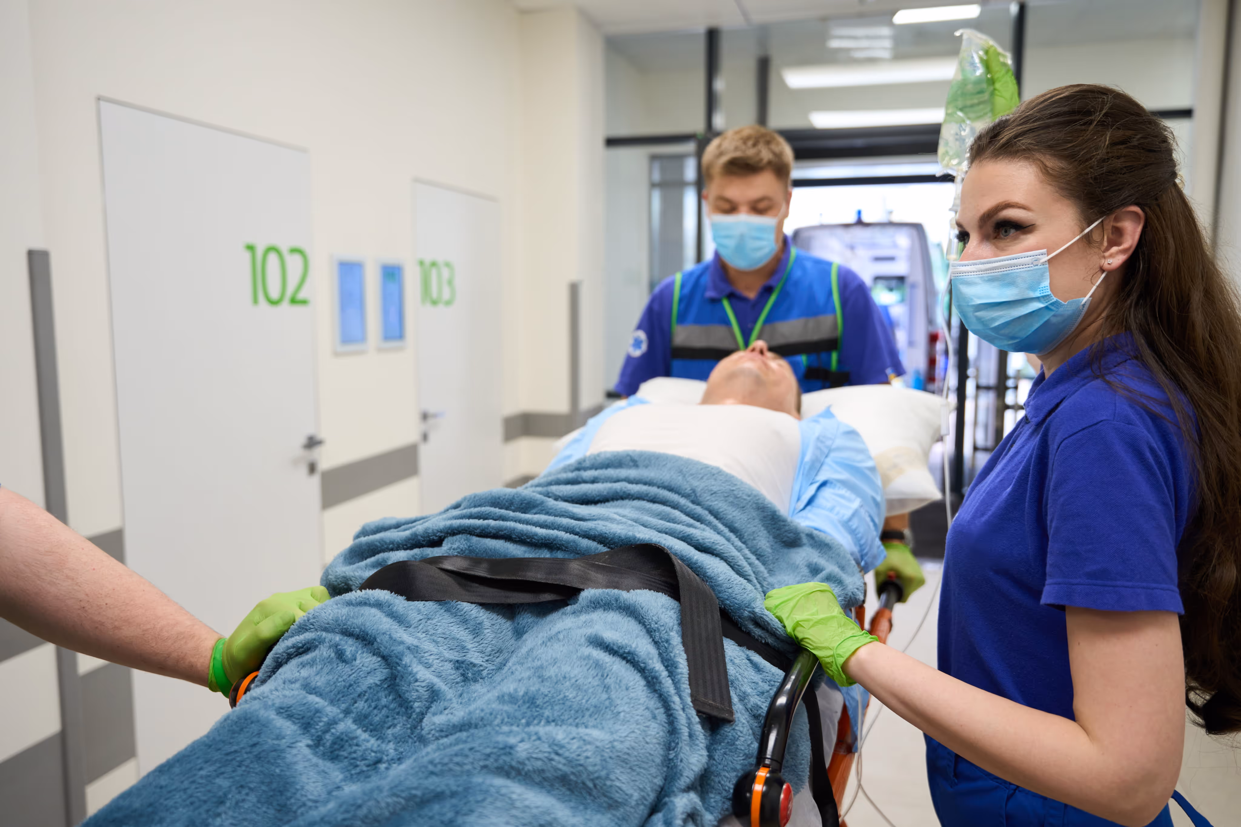 Medical staff wearing masks and gloves transport a patient on a stretcher covered with a blue blanket.