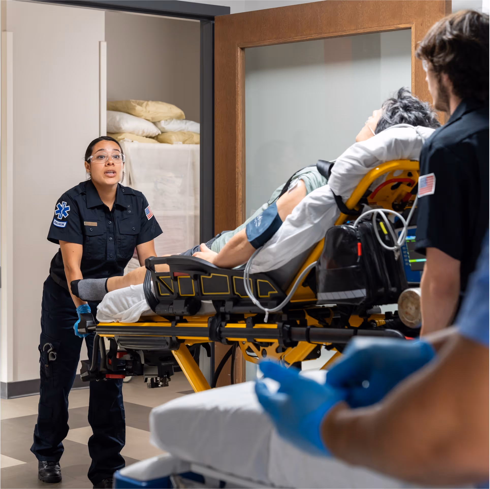 Paramedics in uniform wheeling an injured person on a stretcher into a hospital emergency room.
