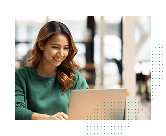 Woman in green sweater smiling while working on a laptop indoors with blurred background.