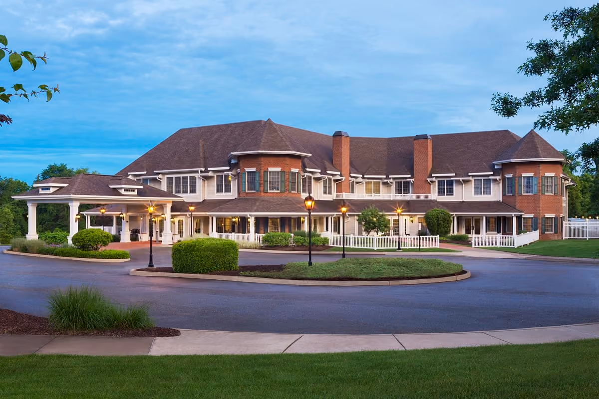 Large two-story residential building with brick accents, wrap-around porch, and lamp posts in front.