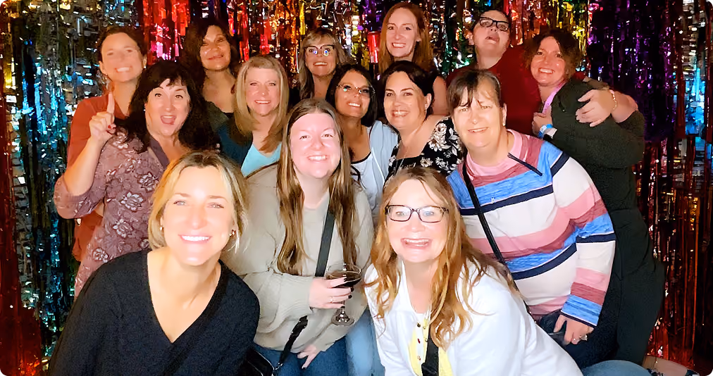 Group of happy women posing together in front of colorful shiny backdrop at a party.