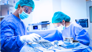 Two surgeons in blue scrubs and masks preparing surgical instruments in an operating room.