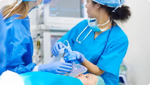 Medical staff in scrubs and gloves preparing a patient with an anesthesia mask before surgery.