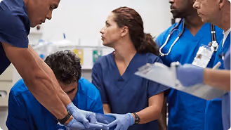 A team of four medical professionals in blue scrubs and gloves closely attending to a patient in a clinical setting, focused on urgent care.