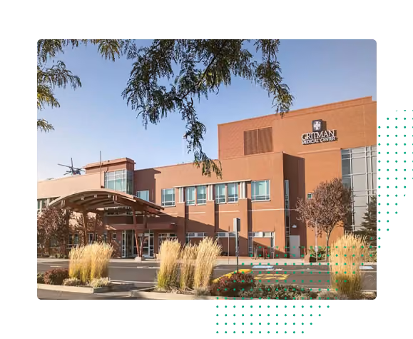 Exterior view of the Critman Medical Center building with a covered entrance, framed by ornamental grasses and trees under a clear blue sky.