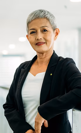Confident older woman with short gray hair wearing a black blazer and white top, standing indoors and smiling at the camera.