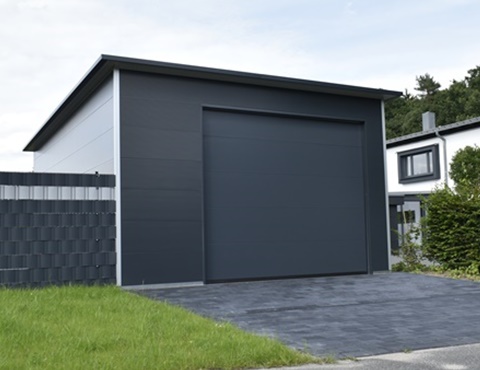 Anthrazitfarbene Fertiggarage mit Flachdach aus wärmegedämmten Sandwichpaneelen, modernem Design und gepflasterter Einfahrt