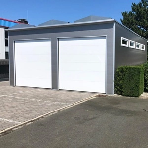 Moderne Wohnmobilgarage aus langlebigen Sandwichpaneelen mit weißen Sektionaltoren und seitlichen Oberlichtern, umgeben von gepflegtem Garten