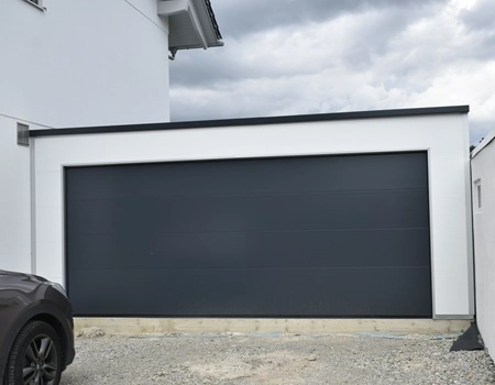Doppelgarage aus Sandwichpaneelen mit weißer Fassade und anthrazitfarbenem Sektionaltor, wärmegedämmt, wärmedämmend und modern gestaltet. Als Anbaugarage dargestellt