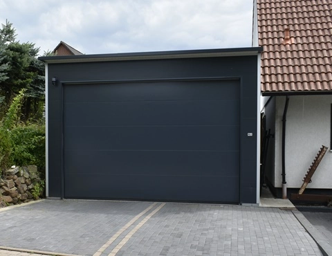 Moderne Anbaugarage mit Flachdach aus wärmegedämmten Sandwichpaneelen und anthrazitfarbenem Sektionaltor – energieeffiziente Lösung direkt am Wohnhaus