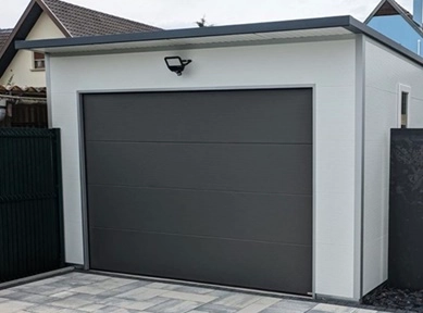 Freistehende Einzelgarage aus wärmedämmenden Sandwichpaneelen mit weißer Fassade, anthrazitfarbenem Sektionaltor und modernem Flachdach für Pkw