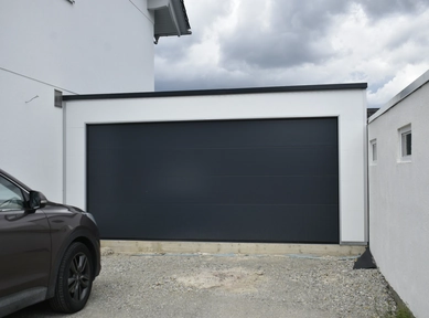 Doppelgarage aus Sandwichpaneelen mit weißer Fassade und anthrazitfarbenem Sektionaltor, wärmegedämmt und modern gestaltet