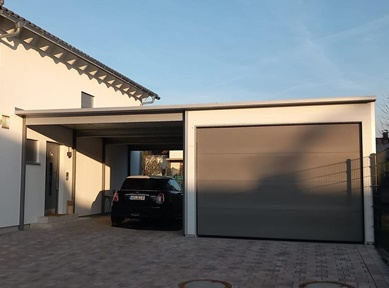 Moderne Anbaugarage mit Carport-Kombination aus wärmedämmenden Sandwichpaneelen, weißer Fassade und grauem Sektionaltor – praktische Lösung für Pkw-Stellplätze