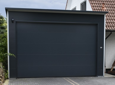 Freistehende Einzelgarage aus wärmedämmenden Sandwichpaneelen mit anthrazitfarbenem Sektionaltor und Flachdach für Pkw