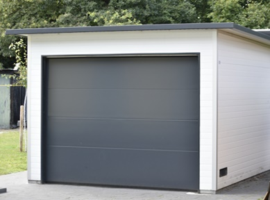 Freistehende Einzelgarage aus wärmedämmenden Sandwichpaneelen mit weißer Fassade und anthrazitfarbenem Sektionaltor, moderne Lösung für Pkw