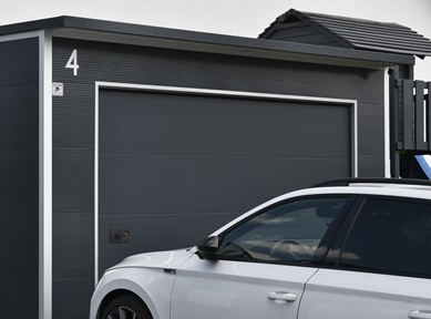 Moderne Designgarage aus wärmedämmenden Sandwichpaneelen mit anthrazitfarbenem Sektionaltor und Flachdach, angebaut an ein Wohnhaus, ideale Lösung für Pkw