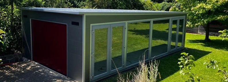 Sonderanfertigung einer modernen Fertiggarage aus wärmedämmenden Sandwichpaneelen mit rotem Sektionaltor, großen Glasfronten und Doppeltüren – vielseitig nutzbar für Pkw und zusätzlichen Wohn- oder Arbeitsraum