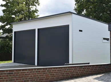 Weiße Doppelgarage aus wärmedämmenden Sandwichpaneelen mit zwei anthrazitfarbenen Sektionaltoren und modernem Flachdach. Ideal für Wohnmobile oder Gewerbefahrzeuge wie Feuerwehrfahrzeuge oder Krankenwagen