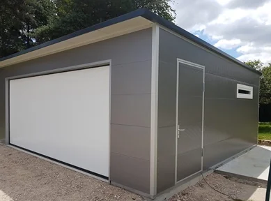 Moderne Einzelgarage aus wärmedämmenden Sandwichpaneelen in Grau mit weißem Sektionaltor, seitlicher Zugangstür und Fenster – praktische Lösung für Pkw